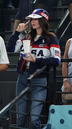 a woman holding a coffee cup while standing next to a man in a baseball cap