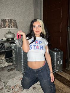 a woman in jeans and a crop top is posing for the camera while holding a water bottle