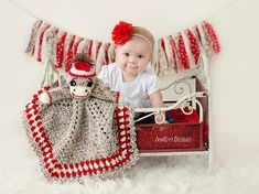 a baby sitting in a crocheted bed next to a stuffed monkey and blanket