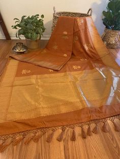 Blended Silk (cotton & silk) in a beautiful tawny brown shade with golden floral motifs all over the length of the saree and solid gold zari border. The fabric is a blend of cotton and silk- very soft and comfortable. It has a fall like crepe and looks just as royal as a benarasi.Condition: NewFabric: Cotton & SilkLength: 5.5 metres Fall & Pico : Saree comes with fall and pico Blouse: Saree comes with running blouse piece that is already cut. Customized stitching: available upon requ Transitional Gold Cotton Silk Dupatta, Brown Traditional Wear With Traditional Patterns, Festive Brown Traditional Wear For Ceremonies, Brown Traditional Wear With Cutdana For Puja, Brown Traditional Drape For Puja, Brown Traditional Wear For Puja, Traditional Brown Cutdana Wear, Festive Brown Traditional Wear With Traditional Patterns, Traditional Brown Saree With Cutdana