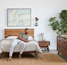 a man sitting on top of a bed next to a wooden dresser and nightstands