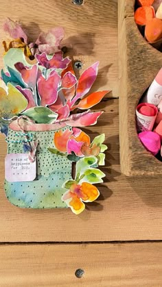 a wooden table topped with lots of crafting supplies next to a vase filled with flowers