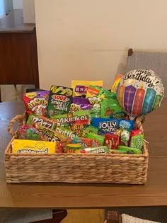 a basket filled with candy and balloons sitting on top of a wooden dining room table