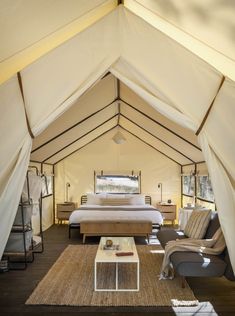 a bed sitting inside of a white tent next to a couch and coffee table on top of a wooden floor