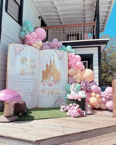 an open book sitting on top of a wooden platform next to balloons and flowers in front of a house