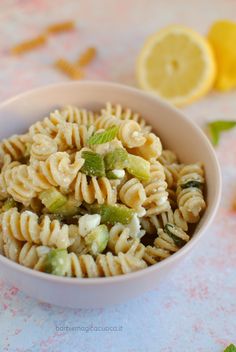 a white bowl filled with pasta salad next to sliced lemons and mint leaves on a table