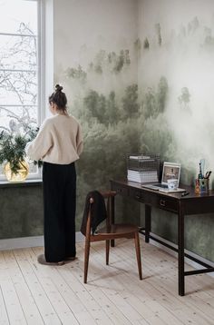 a woman standing in front of a desk next to a window