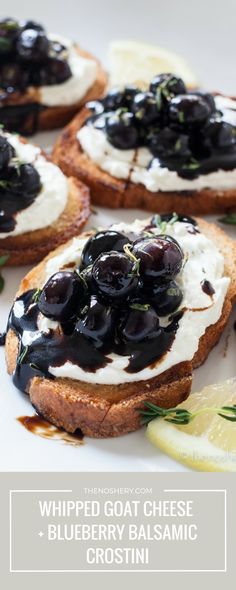 a white plate topped with bread covered in black olives and cream cheese next to lemon wedges