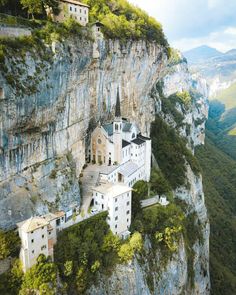 an old church perched on the side of a steep cliff in europe, surrounded by greenery