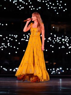 a woman in a yellow dress singing into a microphone on stage with lights behind her