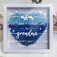 a blue heart shaped shadow in a white frame with the words first mom and grandma written on it