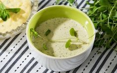 a green cup filled with soup and garnished with parsley on a black and white striped tablecloth