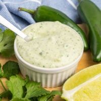 a small white bowl filled with green sauce next to sliced limes and cilantro