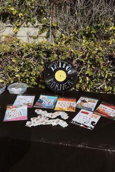 a table topped with lots of cards next to a black cloth covered wall and shrubbery