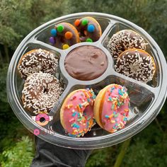 a person holding up a tray with donuts and chocolate frosting on it in front of trees