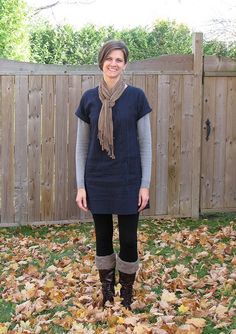 a woman standing in front of a fence with leaves on the ground and wearing boots