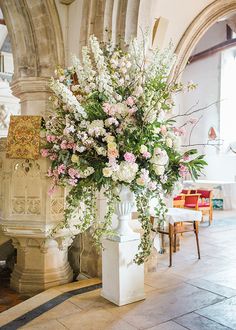 a vase filled with lots of flowers sitting on top of a white pedestal next to a wall