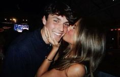 a man and woman kissing each other in front of a tv screen at night time