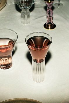 three wine glasses sitting on top of a white tablecloth covered table with plates and utensils