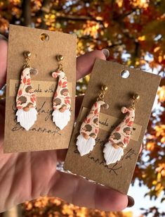 two pairs of earrings are shown in front of a tree with leaves and flowers on it