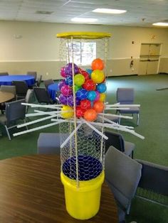 a yellow bucket filled with lots of colorful balls on top of a table in a room