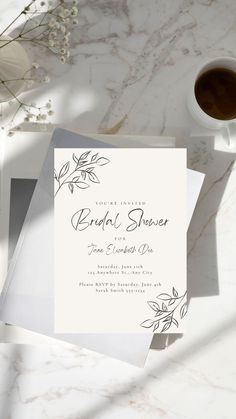 the wedding stationery is laid out next to a cup of coffee and some flowers