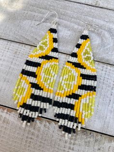 a pair of yellow and black beaded earrings on top of a wooden table next to a