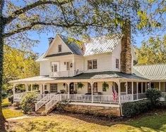 a large white house sitting on top of a lush green field next to a forest