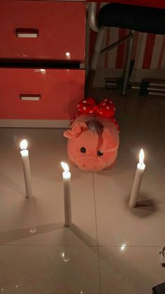 a pig with a bow on its head sitting in front of three candles that are lit