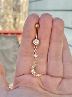 a person holding a gold belly button with a crescent and star dangling from it