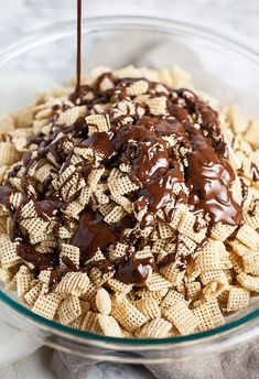 a glass bowl filled with chocolate and cheetos cereal mix, drizzled with chocolate