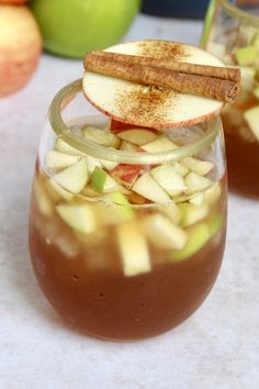 two glasses filled with apple cider and cinnamon sticks on top of each glass next to apples