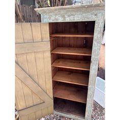 an old wooden bookcase with doors open on gravel ground in front of a fence