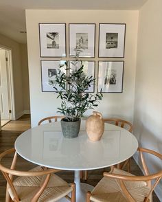 a white table with four chairs and a potted plant on it in front of framed pictures