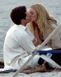 a man and woman kissing on the beach while sitting next to each other with an umbrella in front of them