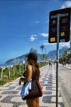 a woman standing on the side of a road next to a street sign and palm trees