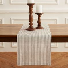 two candles sitting on top of a wooden table next to a white cloth covered candle holder