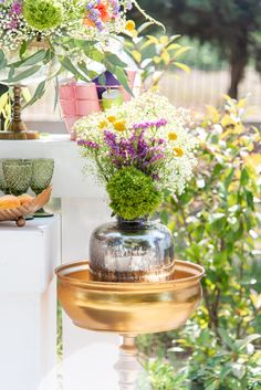 a vase filled with lots of flowers sitting on top of a metal stand next to plants