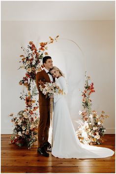 a newly married couple standing in front of an arch with flowers and foliage on it