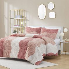 a bed with pink and white comforter in a bedroom next to two mirrors on the wall