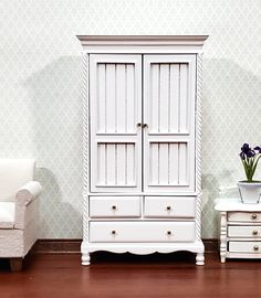 a white armoire sitting on top of a hard wood floor next to a chair