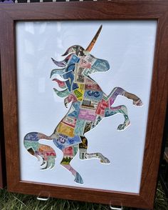 a unicorn made out of different types of money is displayed in a wooden frame on the grass