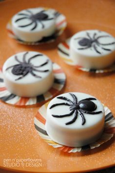 three decorated cookies sitting on top of an orange plate with black spider decorations around them