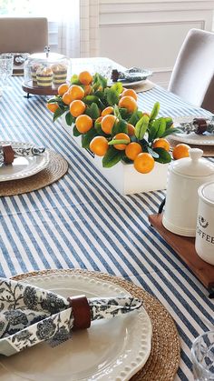 the table is set with plates, napkins and oranges in vases on them