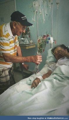 an old man in a hospital bed with flowers on his hand and another person laying down next to him