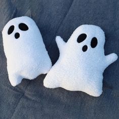 two white ghost pillows sitting on top of a blue sheet covered ground with black eyes