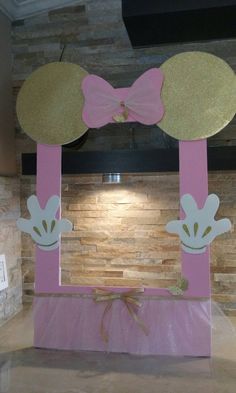 a pink and gold minnie mouse decoration in front of a wall with a bow on it