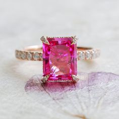 "The radiant cut, cultured pink sapphire at the center of this playful ring represents the color of fiery passion for love and for life. A moissanite hidden halo and encrusted prongs offer just the right amount of sparkle to this feminine and charming ring. Made to order. Please allow 4-6 weeks for delivery. ◊ DETAILS ◊ Center Stone: - Type: Pink Sapphire (cultured) - Size: 8 x 10mm (3.5ct diamond equivalent) - Color: Pink - Cut: Radiant Setting: - Moissanite hidden halo and encrusted prongs - 14K or 18K  - White, yellow, or rose gold - 2 mm wide band - Sits ~8.2 mm (.32\") off the finger ◊ CUSTOMIZATION ◊ Any designs in our current collection can be customized with different stone type, size, color, or cut. Looking for something created just for you? Our bespoke design service can turn yo Pink Engagement Ring, Pink Sapphire Ring Engagement, Pink Sapphire Ring, Hidden Halo, Personalized Gifts For Her, Radiant Cut, Pink Ring, Sapphire Stone, Sapphire Jewelry