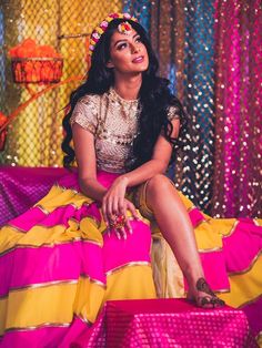 a woman sitting on top of a pink and yellow bed in front of colorful curtains