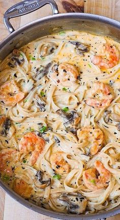 a pan filled with pasta and shrimp on top of a wooden table